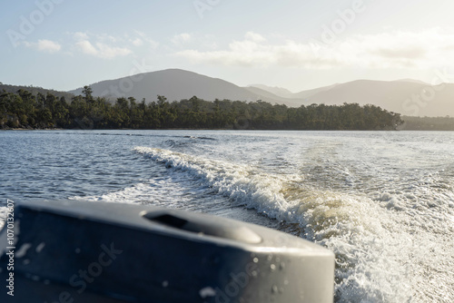 tinny dinghy boat on the water making a wake behind a boat making waves on a river in a national park in australia. beach in summer, dingy going fast photo