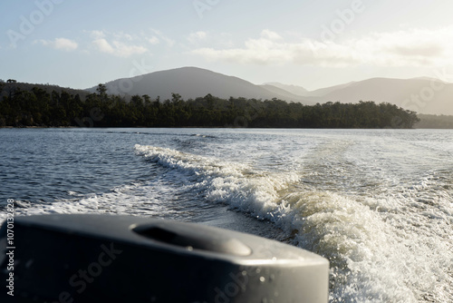 tinny dinghy boat on the water making a wake behind a boat making waves on a river in a national park in australia. beach in summer, dingy going fast photo