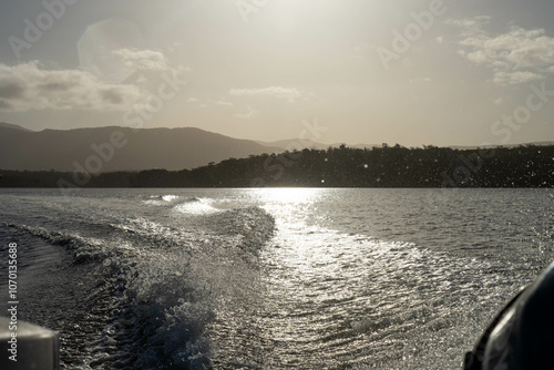 tinny dinghy boat on the water making a wake behind a boat making waves on a river in a national park in australia. beach in summer, dingy going fast photo