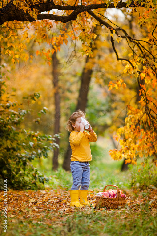 Three year old girl having breakfast in autumn park, drinking tea from a cup with a basket of food and fruit nearby Three year old girl having breakfast in autumn park, drinking tea from a cup with a basket of food and fruit nearby