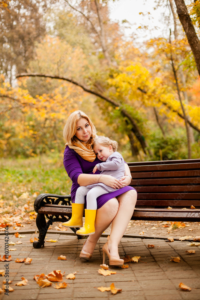 Plus-size woman in purple dress gently hugging her crying 3-year-old daughter on a bench in an autumn park Plus-size woman in purple dress gently hugging her crying 3-year-old daughter on a bench in an autumn park