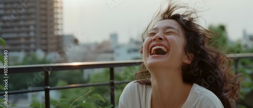 A laughing individual on a city balcony, hair tousled by the breeze, radiates genuine joy amidst an urban backdrop. photo