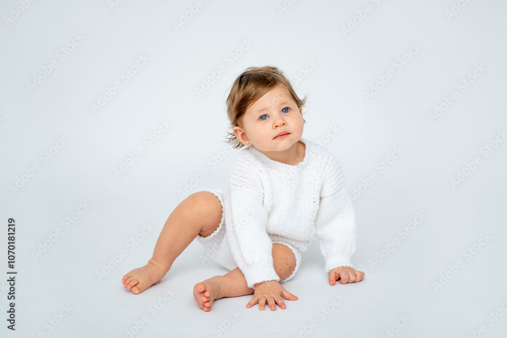 A baby boy on a white isolated background with a place for text is sitting in white knitted clothes. A small happy child in a winter sweater looks at the top or to the side, a space for text A baby boy on a white isolated background with a place for text is sitting in white knitted clothes. A small happy child in a winter sweater looks at the top or to the side, a space for text