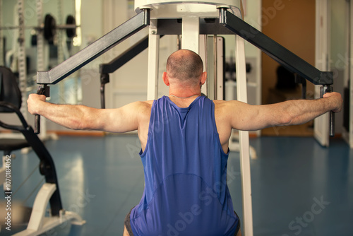 Male athlete exercises on a strength training machine in a gym. Back view. photo