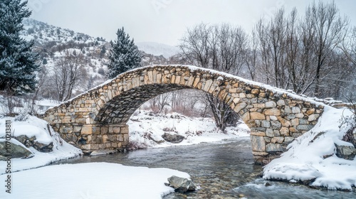 A stone arch bridge spans a river in a snowy mountain landscape. photo