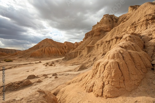 Scenic view of an arid desert with eroded clay formations under a dramatic cloudy sky, showcasing natural textures and raw beauty of a dry, rugged terrain.