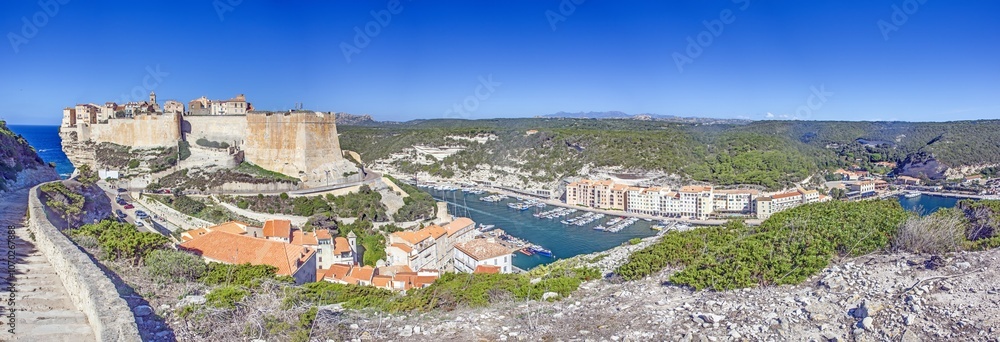 Naklejka premium Historic Bonifacio on Corsica’s dramatic limestone cliffs against a clear blue Mediterranean sea and sky