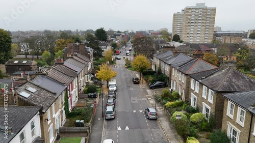 Aerial view of suburban London, showing semi detached houses alongside a residential street, with blocks of high rise social housing in the background.
