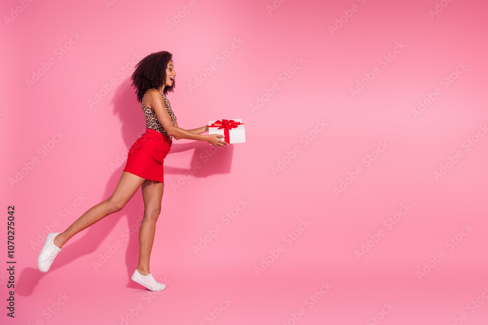 Full size photo of pretty young girl hold gift profile walking wear trendy leopard print outfit isolated on pink color background Full size photo of pretty young girl hold gift profile walking wear trendy leopard print outfit isolated on pink color background