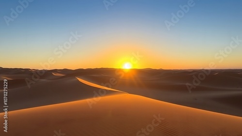 Sunrise in a desert with sand dunes casting long shadows, the sun peeking over the horizon, and a clear blue sky above