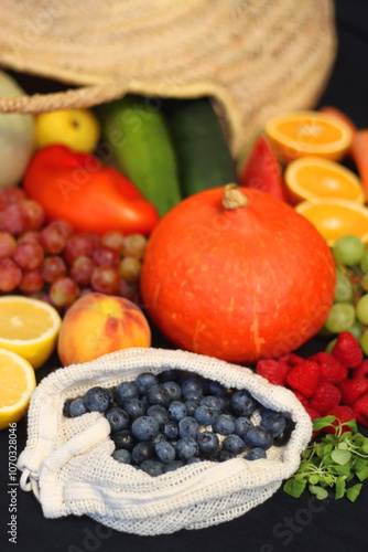 Round straw bag and various seasonal fruits and vegetables on dark background. Summer and fall produce. Selective focus.
