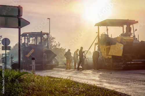 Sunrise Cinematic Scene of Construction Workers and Two Asphalt Pavers Laying New Asphalt for Road Renovation photo