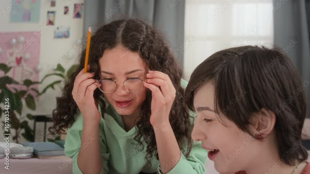 Two teenage girls studying in bedroom, taking notes in workbook, discussing homework and smiling during day at home Two teenage girls studying in bedroom, taking notes in workbook, discussing homework and smiling during day at home