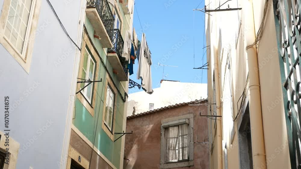 Narrow street in Lisbon, framed by colorful buildings. Washed clothes on the ropes between the old buildings. Narrow street in Lisbon, framed by colorful buildings. Washed clothes on the ropes between the old buildings.