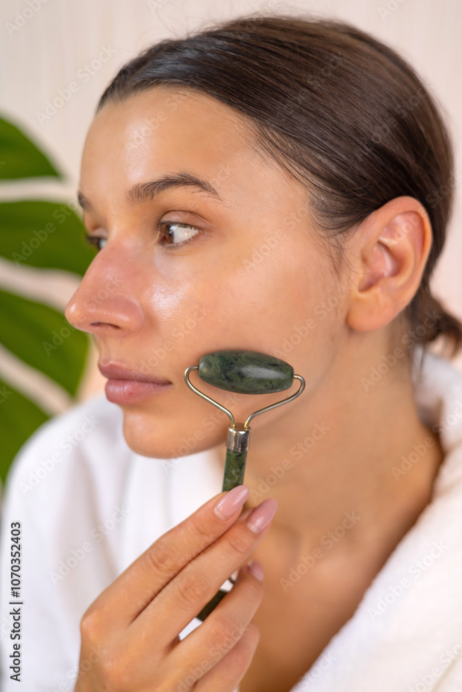 woman applying face sheet mask at home, cream or serum and massaging skin with roller.girl doing beauty routine at home. double side mirror and cream jar on table,monstera plant leaf in background. woman applying face sheet mask at home, cream or serum and massaging skin with roller.girl doing beauty routine at home. double side mirror and cream jar on table,monstera plant leaf in background.