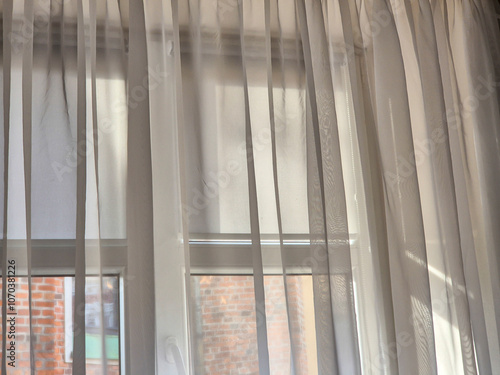 Bright sunlight filtering through sheer white curtains, creating a soft and airy atmosphere in a cozy room.