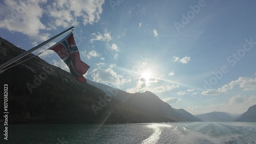 Waving Flag of Norway in Jotunheimen National Park on Sunny Day. Blue Sky and Mountains. Side View from Ferry Stern. Slow Motion