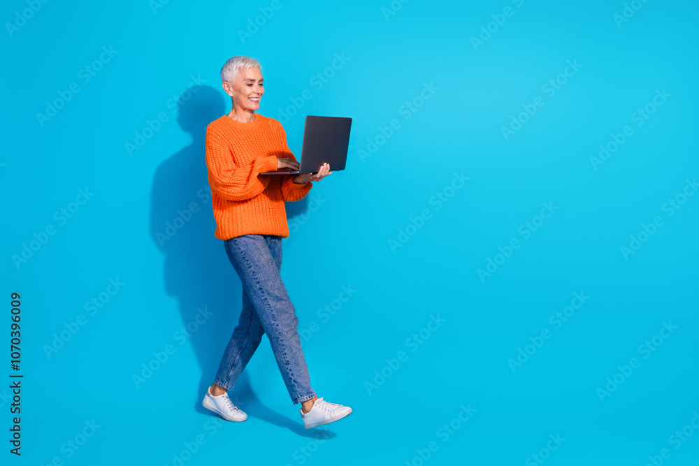 Photo of old positive lady worker walking using netbook texting wear denim jumper isolated blue color background Photo of old positive lady worker walking using netbook texting wear denim jumper isolated blue color background