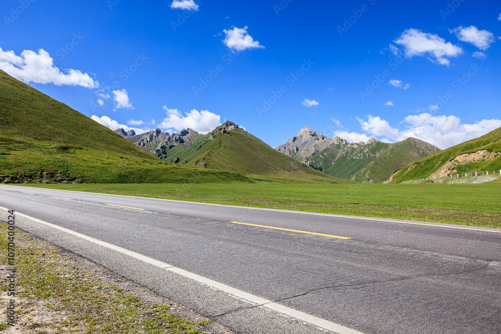 Naklejka premium Countryside asphalt road and green meadow with mountains nature landscape on a sunny day. Road trip.