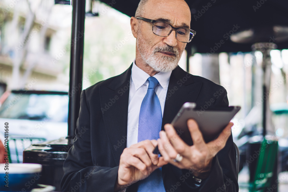 Elderly focused businessman in glasses texting on tablet Elderly focused businessman in glasses texting on tablet