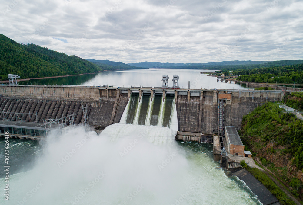 Aerial view of concrete dam releasing water into river on cloudy day. Water discharge at hydroelectric power plant. Aerial view of concrete dam releasing water into river on cloudy day. Water discharge at hydroelectric power plant.