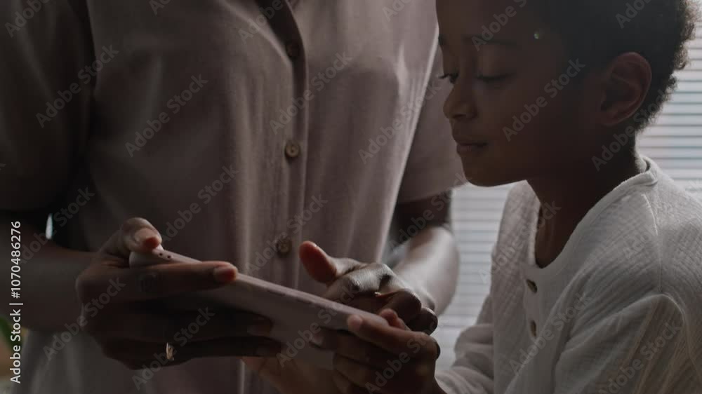 Black boy in linen pajamas laughing while looking at smartphone display during morning routine in bathroom with mom entertaining him with gadget Black boy in linen pajamas laughing while looking at smartphone display during morning routine in bathroom with mom entertaining him with gadget