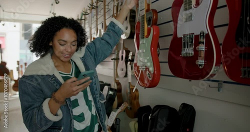 Black Young Adult Female Shopping in Guitar shop and Checking Finances on Phone