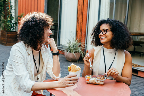 Canvas Print Female colleagues enjoying a lunch break in the office courtyard, sharing smiles