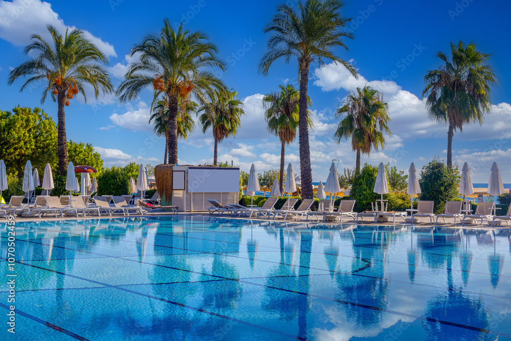 Magnificent view, swimming pool with blue sky with clouds. Holiday hotel in Antalya. Great relaxation and peaceful atmosphere, palm trees, sun loungers reflections.