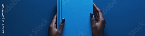 Hands holding blue book on navy background, top view