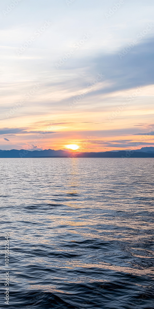 Obraz premium Sunset over calm waters with distant mountains on the horizon during early evening