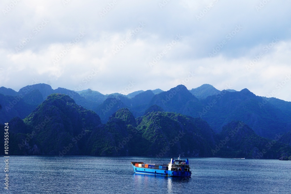Transport morski odbywający się na Filipinach. Duży kontenerowiec płynie w stronę wybrzeża. W tle widać przepiękne tropikalne góry. Transport drogą morską na dużym okręcie.