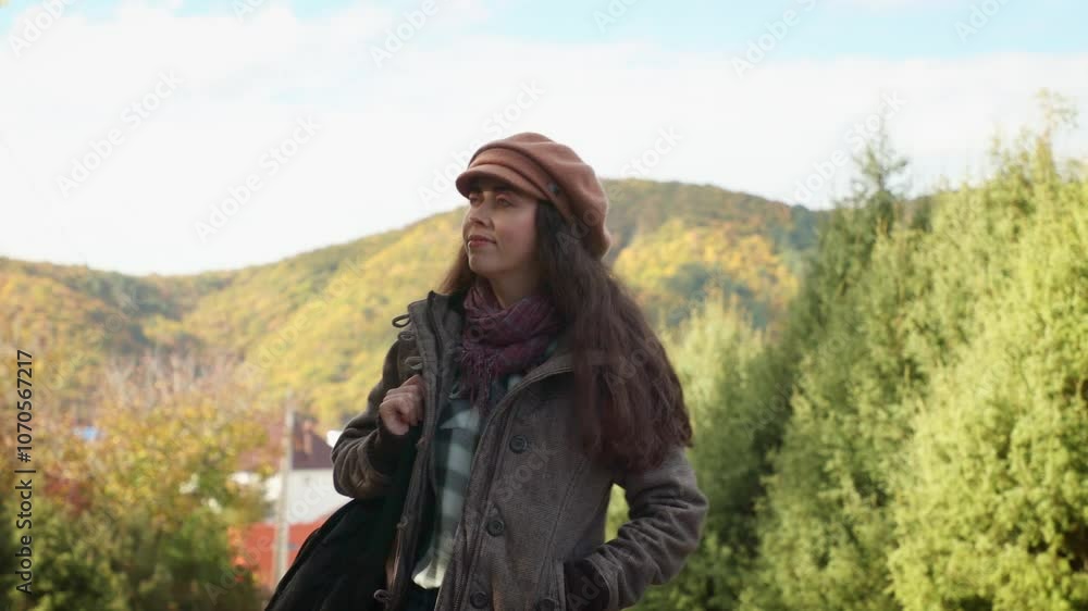 A pretty young Caucasian woman walks through the park with a guitar on her back. There is a mountain view in the background.