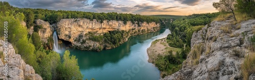 Majestic waterfall cascading into river amidst lush greenery near scenic cliffs during sunset in a tranquil landscape