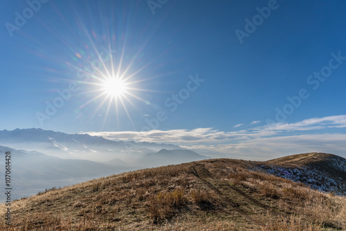 The disk of the sun with rays in the blue sky in the mountains. Traveling around Kyrgyzstan.