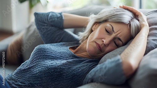 Weak senior woman lie on sofa keep arm on head feel pain dizzy headache suffer from menopause symptoms low blood pressure. Fatigue aged female relax on soft pillow sleep at daytime too tired from heat photo