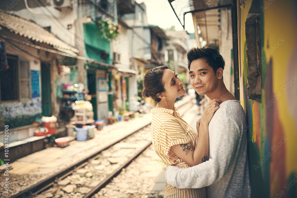 Fototapeta premium City, railway and couple in portrait for hug, travel adventure or explore vacation for anniversary. Interracial marriage, woman and man with romance for admiration, love or bonding outdoor in Vietnam