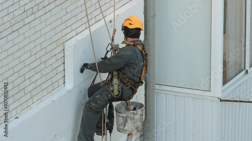 Builder working at height while holding on a rope and insurance. Climber are working on the insulation of facades of a multi-storey residential building.