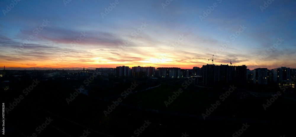 Fototapeta premium Sun goes down. Early morning scene with silhouette dark city. Beautiful colors of sky captured during sunset from Ivano frankivsk, Ukraine.