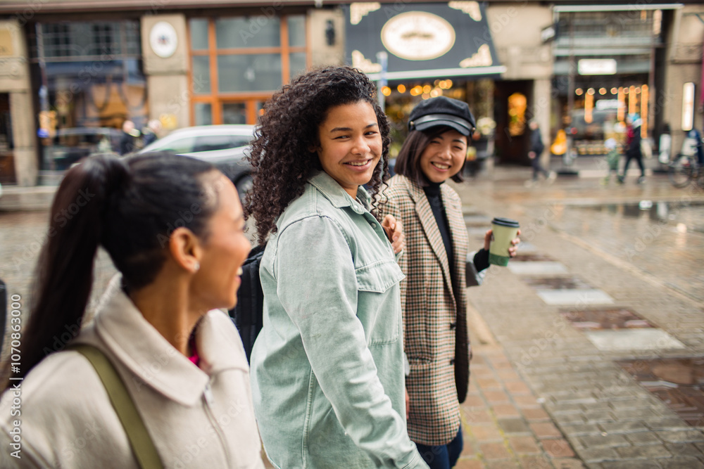 Three stylish women walking and laughing together on a city street with coffee Three stylish women walking and laughing together on a city street with coffee