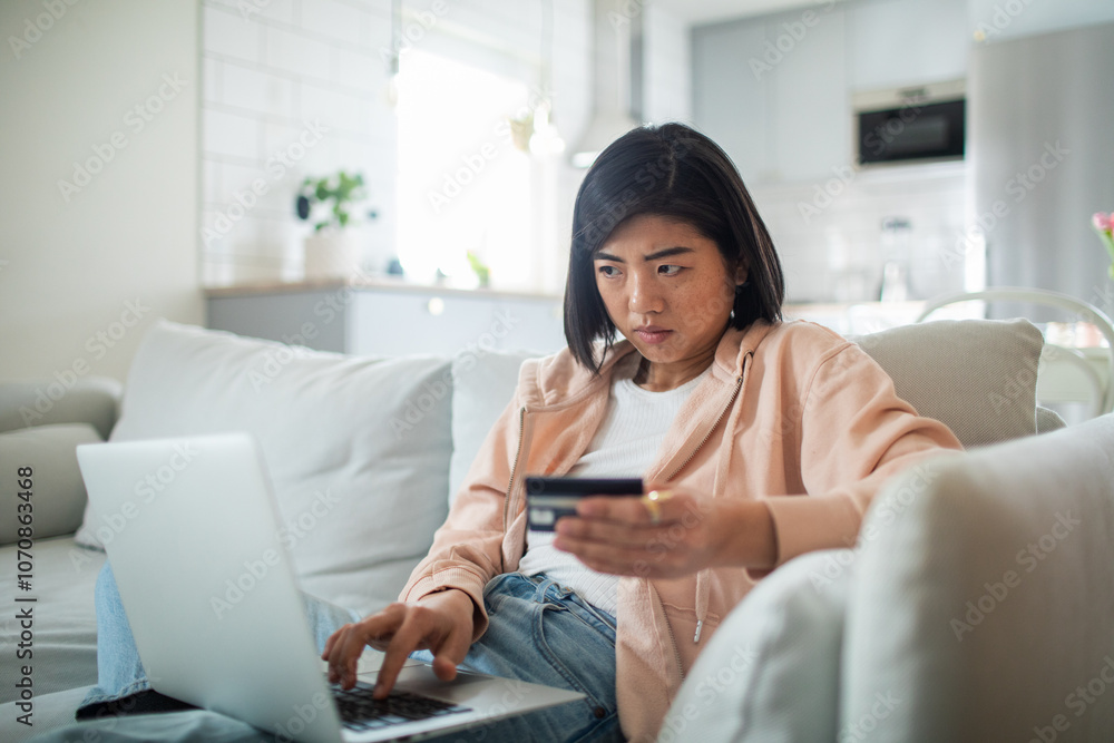 Asian woman using credit card on laptop from home couch Asian woman using credit card on laptop from home couch