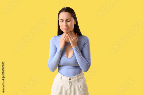 Young woman suffering from sore throat on yellow background