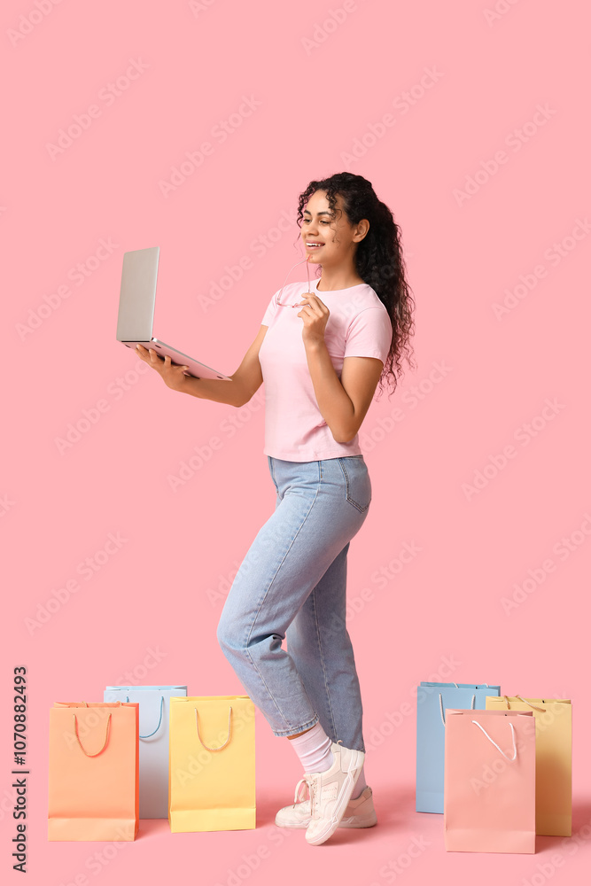 Young woman with credit cards, shopping bags and laptop on pink background Young woman with credit cards, shopping bags and laptop on pink background