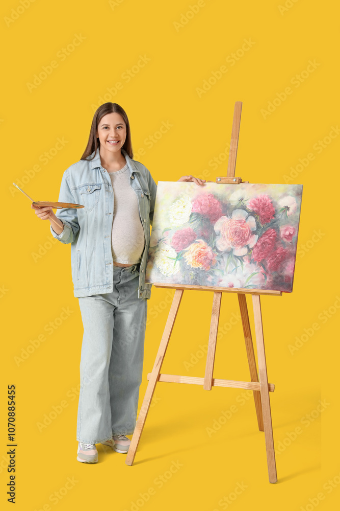Naklejka premium Beautiful female pregnant artist painting on canvas on yellow background