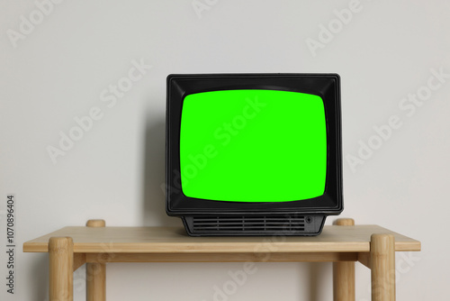 Retro Tv set with green screen on wooden table near white wall, space for design. Chroma key