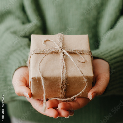 Woman in a green sweater showcasing a sustainable and heartfelt christmas gift wrapped in simple brown paper and twine photo