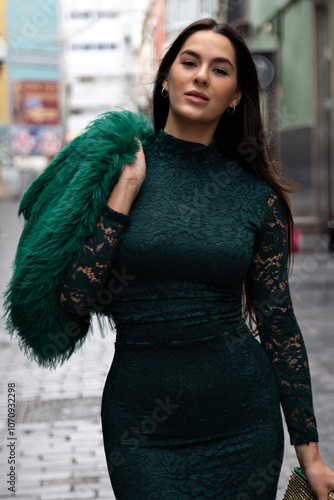 Beautiful fashion model in emerald green lace dress walks down city street photo