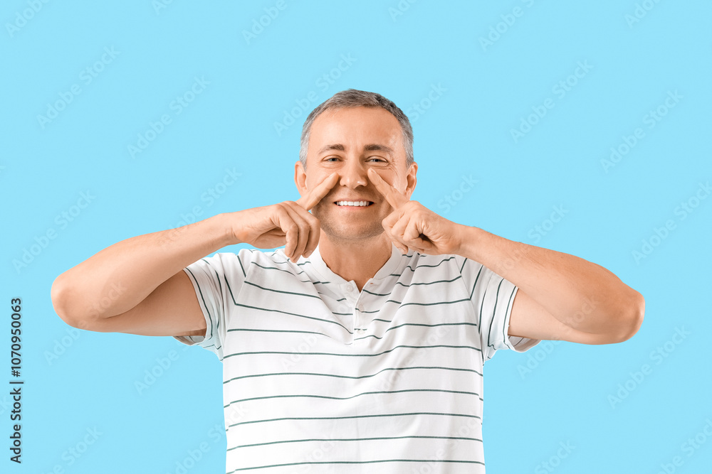 Happy mature man doing face building exercise on blue background Happy mature man doing face building exercise on blue background