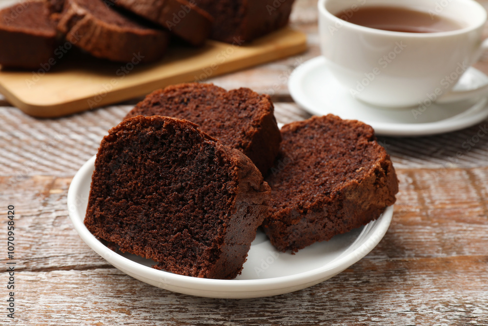 Slices of delicious chocolate sponge cake and tea on wooden table, closeup Slices of delicious chocolate sponge cake and tea on wooden table, closeup