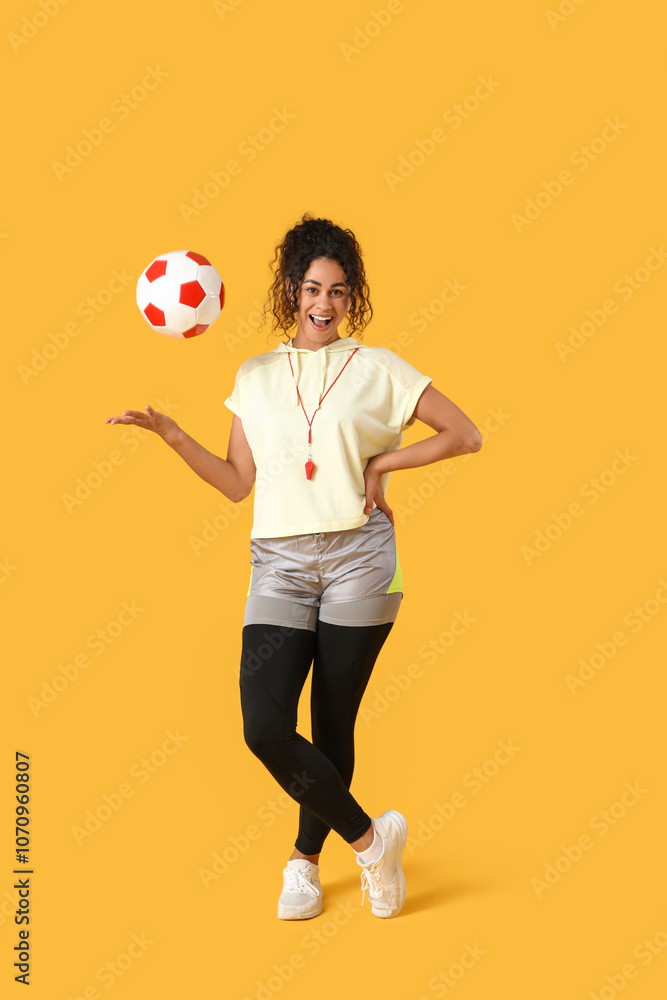 Female African-American soccer trainer with ball on yellow background Female African-American soccer trainer with ball on yellow background